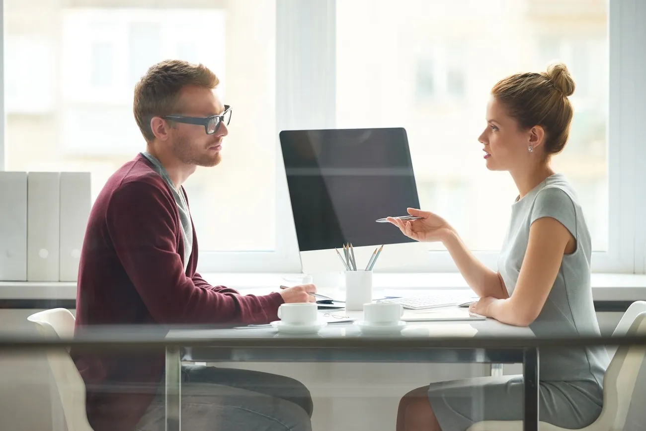 Two professionals engaged in a job interview discussion in a bright office setting with a computer on the table.