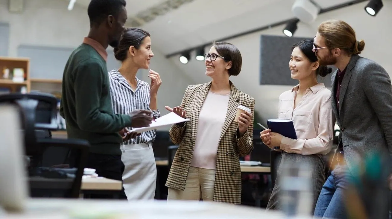 A diverse group of colleagues engaged in a discussion in a modern office setting.