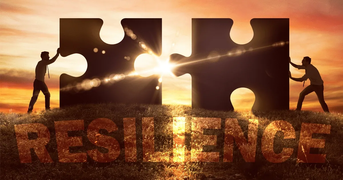 Two businesspeople fit large puzzle pieces together at sunset symbolizing building resilience in the workplace.