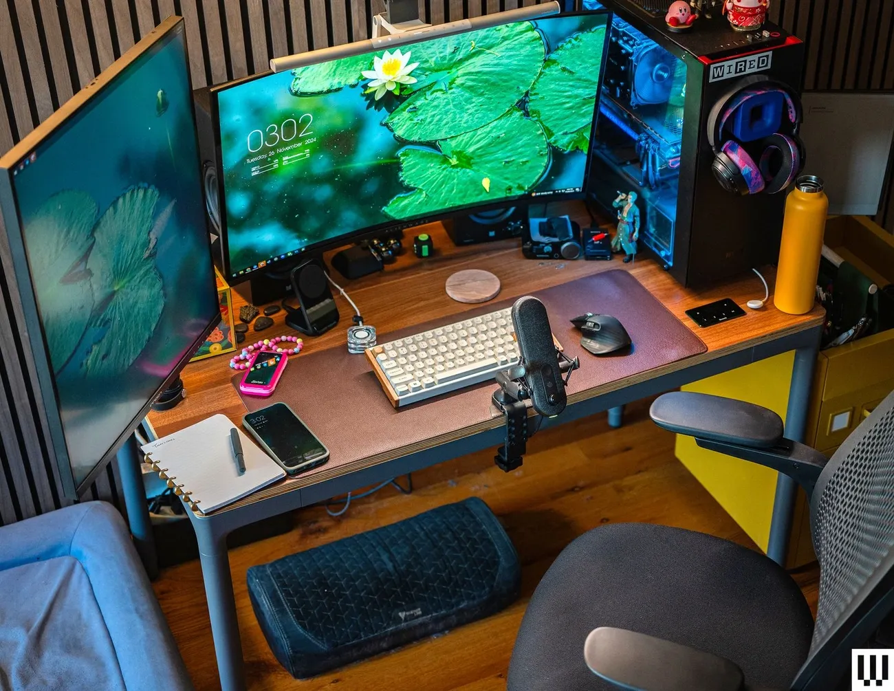 Modern home office setup with dual monitors, mechanical keyboard, microphone, and ergonomic chair on wooden floor